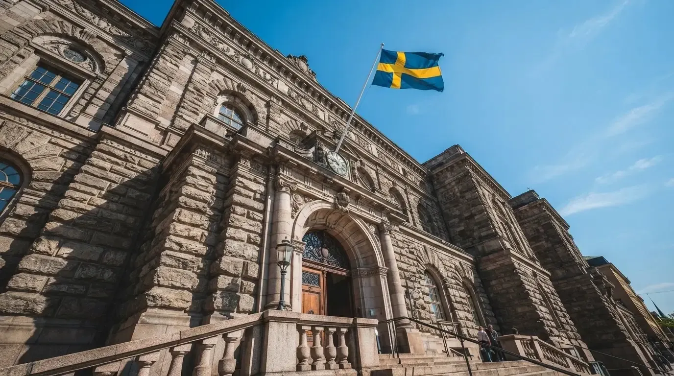 Ett gammalt stadshus i sten fotograferat underifrån mot en klarblå himmel, med den svenska flaggan som fladdrar ovanför entrén.