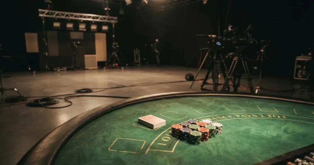 En studiomiljö med ett grönt spelbord, kortlekar och marker uppradade, fotograferad i halvskugga utan synliga personer i förgrunden.